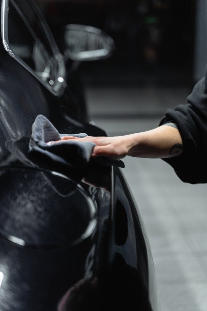 Close-up of a persons hand cleaning a shiny black car with a microfiber cloth in a garage.